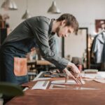 A skilled craftsman meticulously works on leather, showcasing traditional craftsmanship in a well-lit workshop.