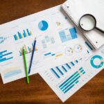 Overhead view of financial charts, magnifying glass, and stationery on wooden table.