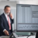 Professional analyzing financial and stock market data on a computer screen in an office setting.